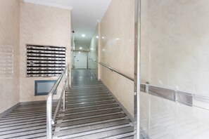 A modern hotel corridor with a metal handrail, a tiled floor, and a wall-mounted mail slot.