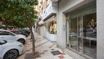 Una acera con autos estacionados, una fachada comercial con un letrero y un árbol.