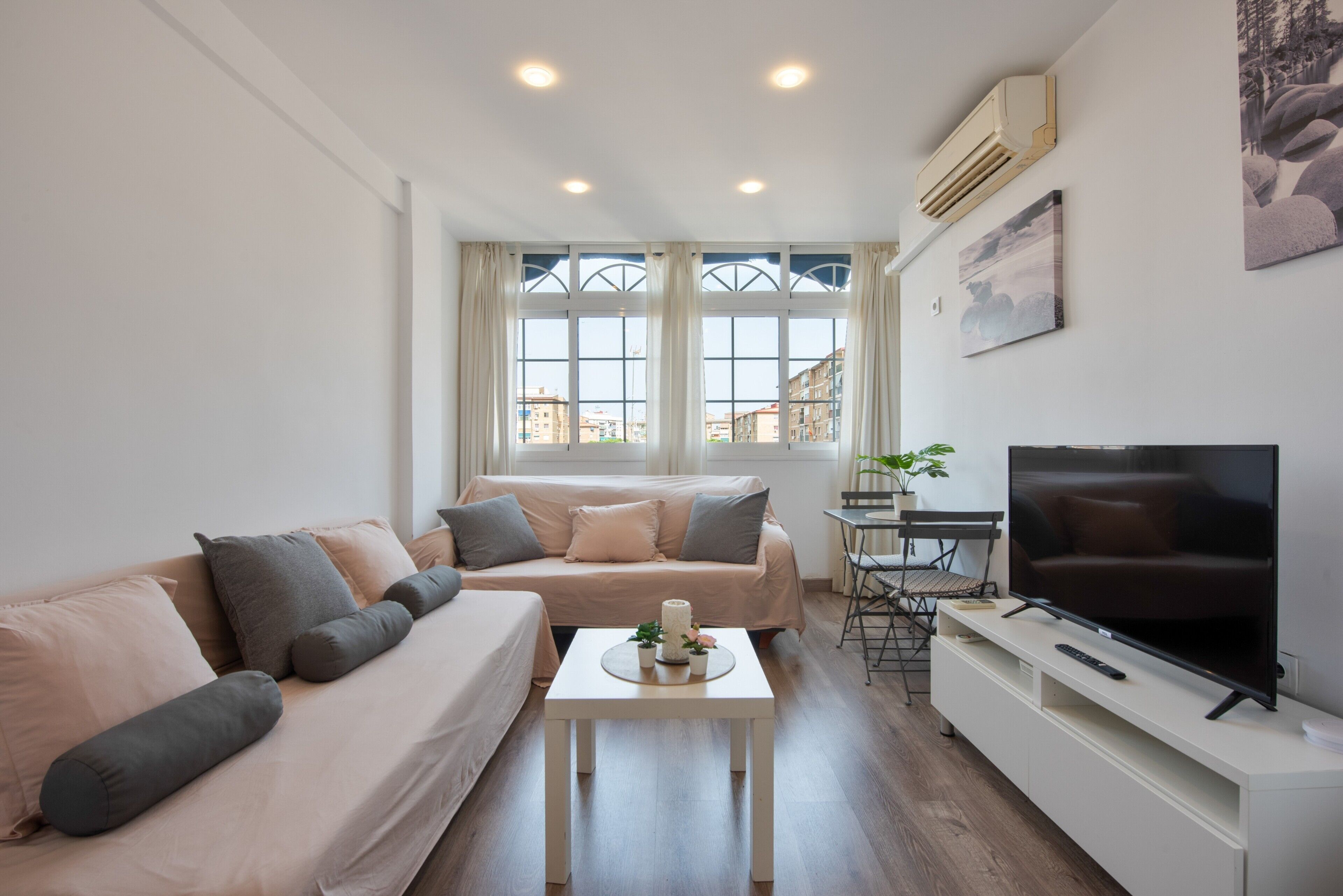 Uma sala de estar moderna com sofá, mesa de centro, televisão e janela com vista para edifícios.