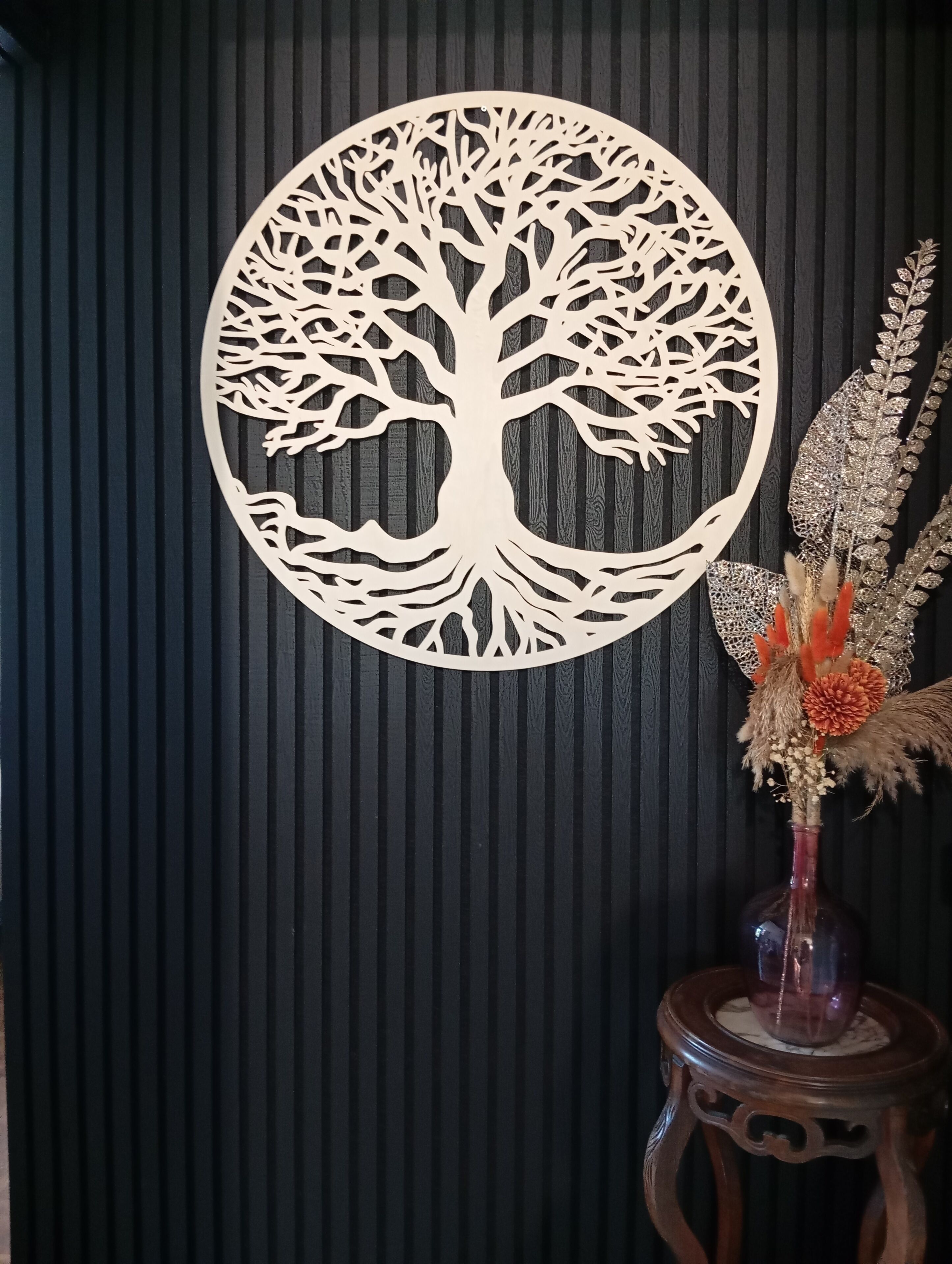 A wall with a circular tree cutout and a vase with dried flowers on a wooden stand.