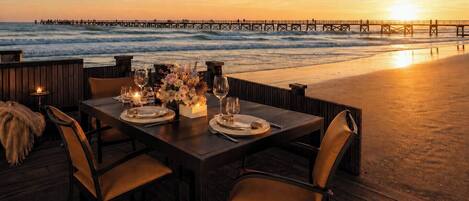 A table set for two with a view of the ocean and a pier in the background.