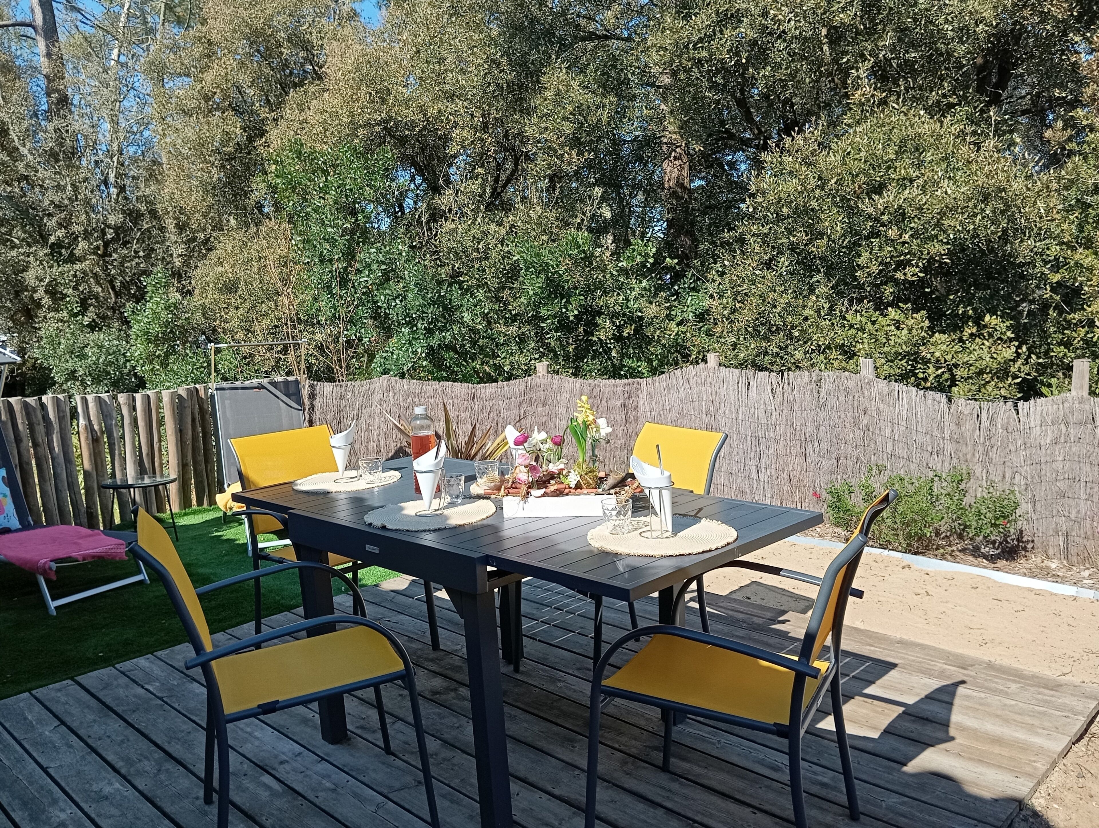 Una terraza exterior con una mesa lista para comer, rodeada de sillas y una valla de madera.