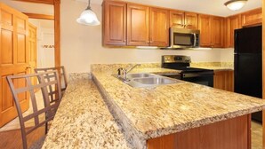 Cocina con armarios de madera, encimeras de granito, electrodomésticos de acero inoxidable e iluminación colgante.