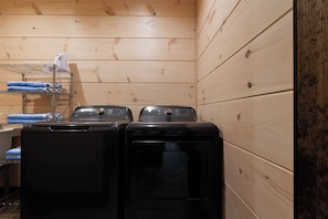 A laundry room with two front-loading washing machines and a metal drying rack with towels. - NEW CABIN: Sauna | Hot Tub | Fire Pit | EV (Gatlinburg)