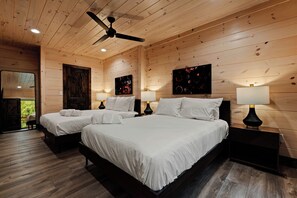 A wooden-paneled room with two beds, a ceiling fan, and artwork on the walls. - NEW CABIN: Sauna | Hot Tub | Fire Pit | EV (Gatlinburg)