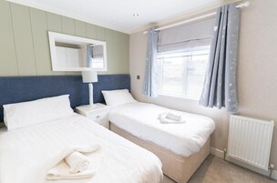 Habitación de hotel con dos camas, una mesita de noche, una lámpara, una ventana con cortinas y un radiador.