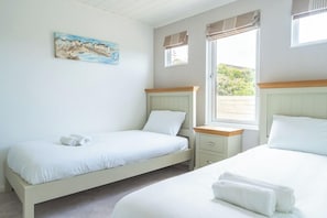 Une chambre avec deux lits, une fenêtre avec des rideaux, un tableau au mur et une petite table de chevet.