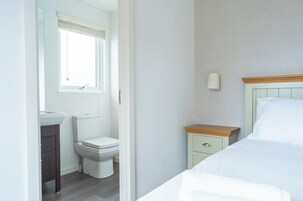 Un dormitorio con cama, mesita de noche, lámpara de pared y ventana con persianas.