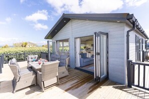 A modern house with a deck, wicker furniture, and a view of the landscape. - Gimblet Rock Holiday Park (Pwllheli)