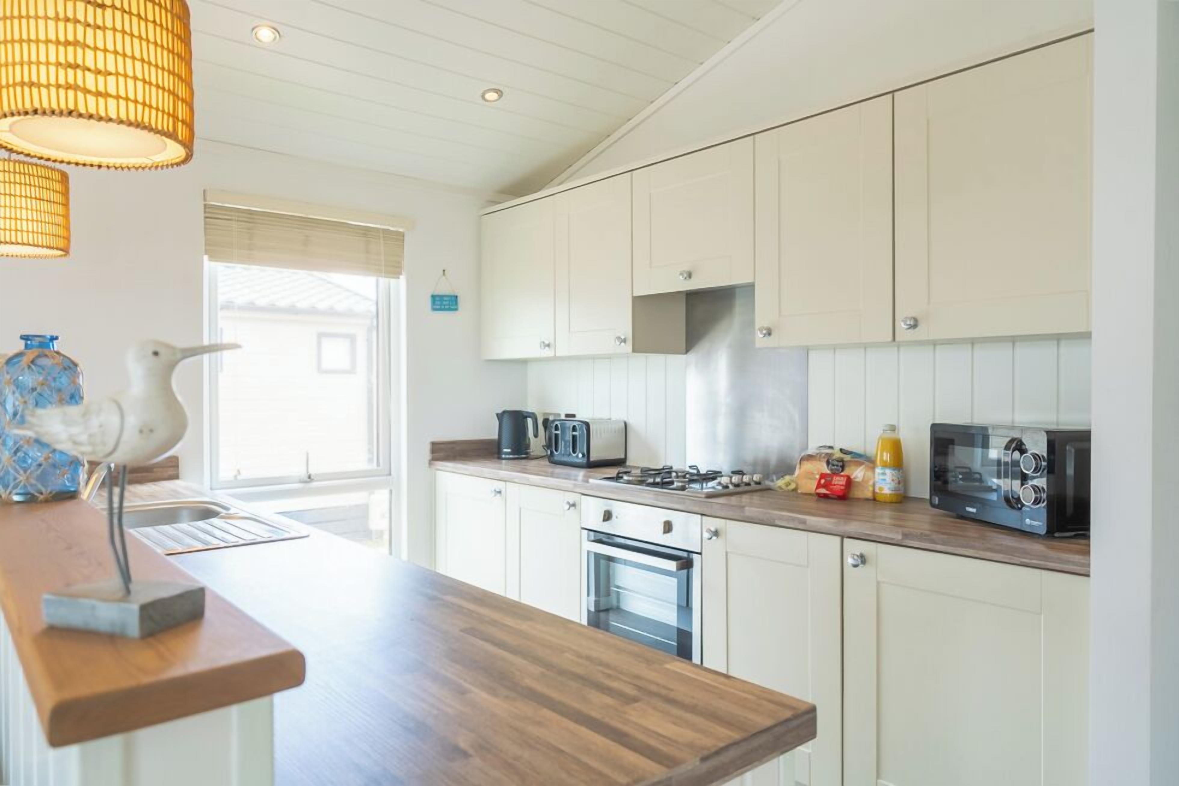 A kitchen with white cabinets, a wooden countertop, a stove, a toaster, and a hanging light fixture.