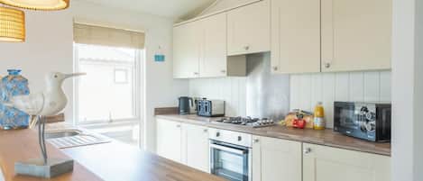 A kitchen with white cabinets, a wooden countertop, a stove, a toaster, and a hanging light fixture.
