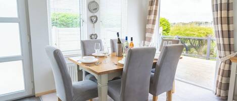 Un comedor con una mesa dispuesta para cuatro personas, sillas, una ventana con persianas y vistas al exterior con vegetación.