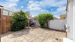A paved patio area with a table and chairs, surrounded by brick walls and greenery. - Cozy 3bd, Garden, Free Parking, M25,bluewater (Dartford)