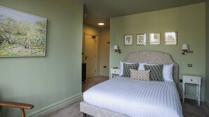A bedroom with a large bed, two bedside tables, a chair, a door, and a painting on the wall.