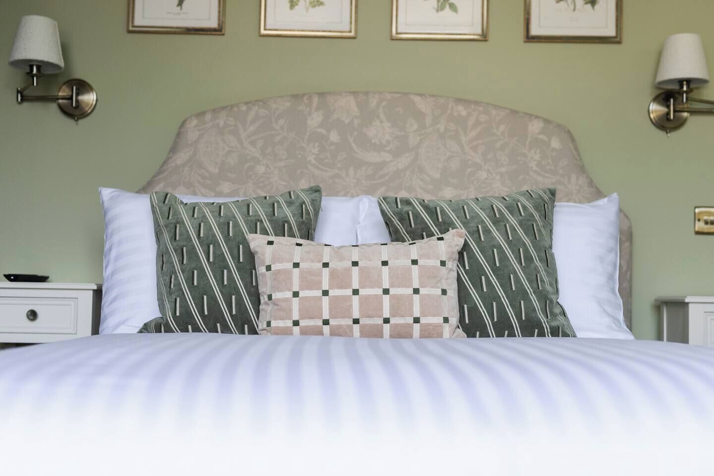 A bed with patterned pillows, a headboard with a floral design, and wall-mounted lamps.