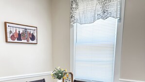 A dining area with a wooden table and chairs, a vase with flowers, and a window with blinds. - Good Vibes & Trail Rides! Cozy 2-bedroom home just off the Chief Ladiga Trail! (Weaver)