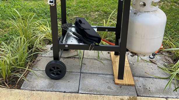 A portable barbecue grill with three burners, a gas tank, and a side table with a brush and cloth. - Good Vibes & Trail Rides! Cozy 2-bedroom home just off the Chief Ladiga Trail! (Weaver)