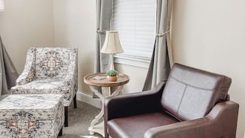 Ein Zimmer mit einem braunen Ledersessel, einem gemusterten Sessel und einem kleinen runden Tisch mit Lampe und Pflanze.