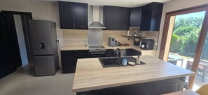 Een moderne keuken met zwarte kastjes, een roestvrijstalen koelkast, een inbouwoven en een groot keukenblok met een spoelbak.