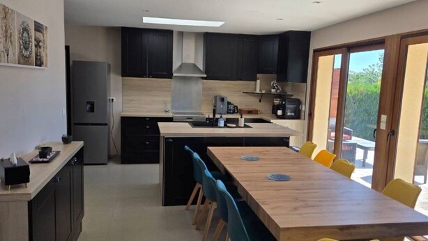 Una cocina moderna con una isla central, armarios negros y una zona de comedor con sillas.