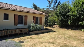 Ein einstöckiges Haus mit Ziegeldach, Holzhörnern und einem kleinen Garten mit einem Holzpflanzkübel und einer Bank.