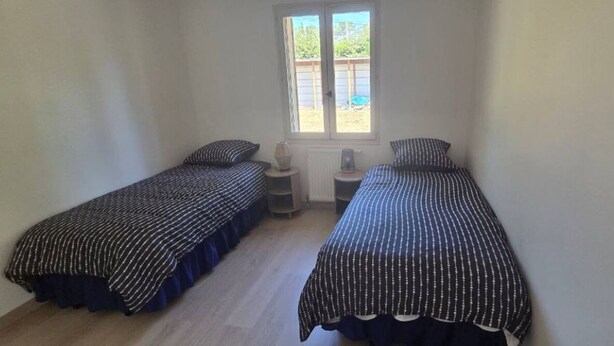 Ein kleines Zimmer mit zwei Einzelbetten, einem Fenster und einer Heizung.