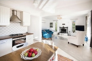 Een moderne keuken met witte kastjes, een gasfornuis en een eethoek met een tafel en stoelen.