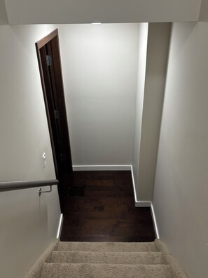 Un escalier étroit, avec une petite plateforme recouverte de moquette, mène à un plancher en bois sombre.