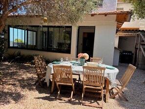 An outdoor dining area with a table set for four, surrounded by wooden chairs, under a tree. - Villa Apolline · 1892 Estate · 5 BR, Heated Pool, Riviera Views (Grasse)