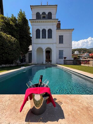 Una piscina con una botella de champán, un paño rojo y un edificio con ventanas de arco y un balcón.