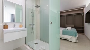 A modern bathroom with a glass shower enclosure, a white sink with a mirror, and a bed with a teal blanket. - Apartment in Las Palmas Near Las Canteras Beach (Las Palmas de Gran Canaria)