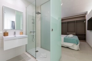 Ein modernes Badezimmer mit Duschkabine aus Glas, einem weißen Waschbecken mit Spiegel und einem Bett mit türkisfarbener Decke.