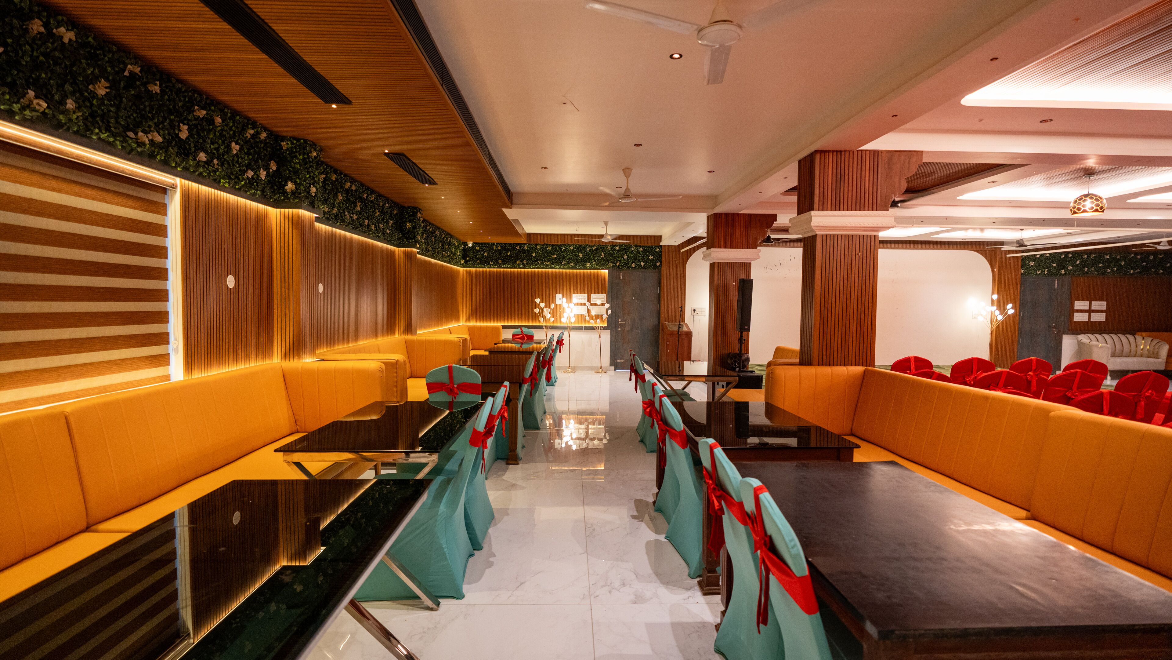 Un vestíbulo de hotel con una larga recepción, zonas de estar con sillas rojas y verdes, y un diseño de techo moderno.
