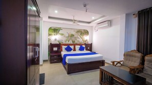 Habitación de hotel con una cama, una mesita de noche de madera, un escritorio, una silla, un ventilador de techo y aire acondicionado instalado en la pared.