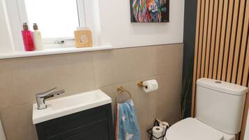A bathroom with a white sink, a toilet, a window with a view, and a shelf with toiletries.