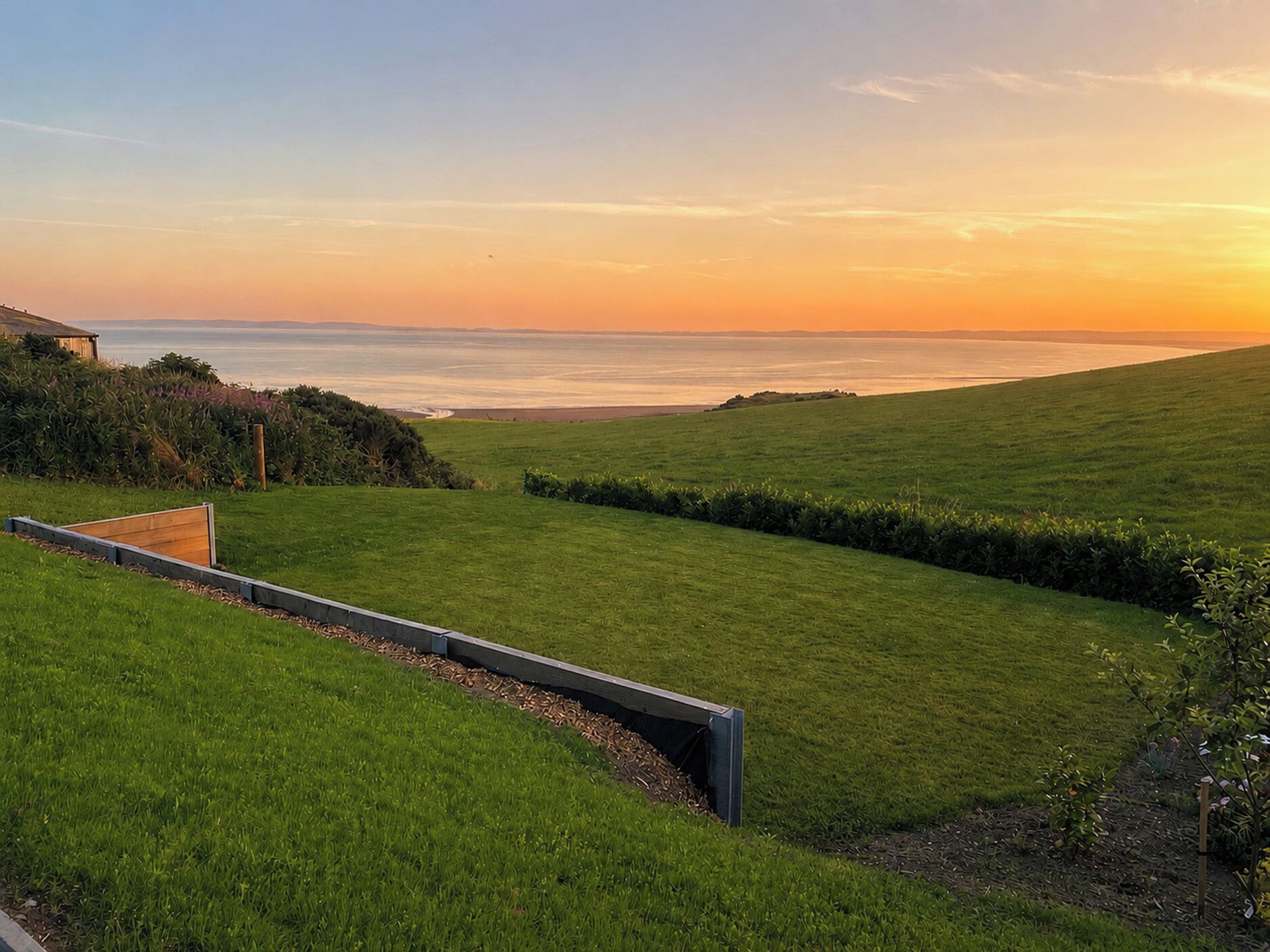 A grassy landscape with a wooden deck and a view of the ocean at sunset.