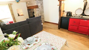 Ein Essbereich mit Tisch für zwei Personen, einer Couch, einem Kamin aus Stein und einer roten Küche mit Herd.