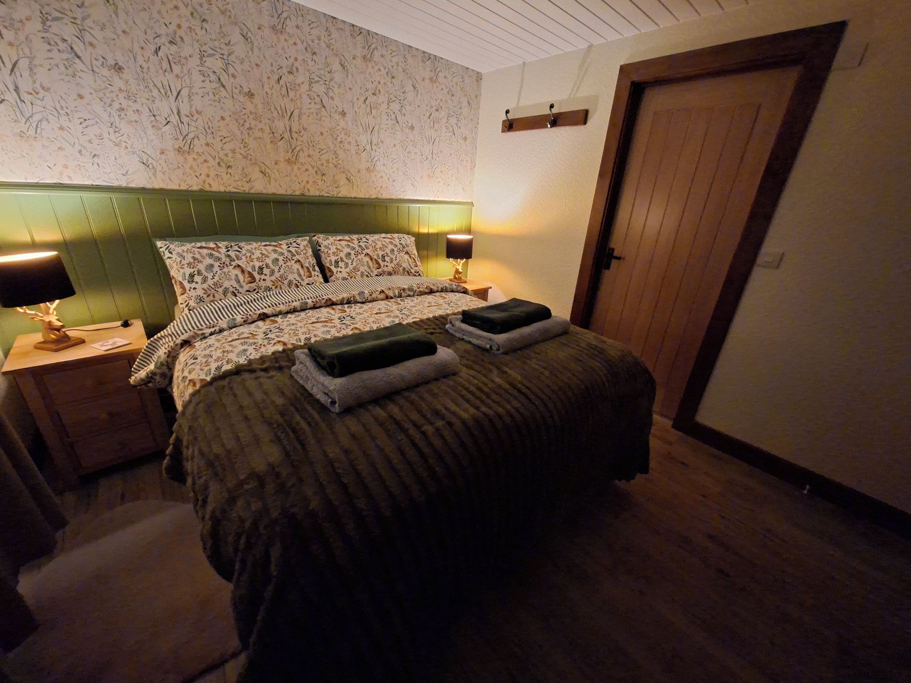 A bedroom with a bed, two bedside tables, a nightstand, a lamp, and a door.