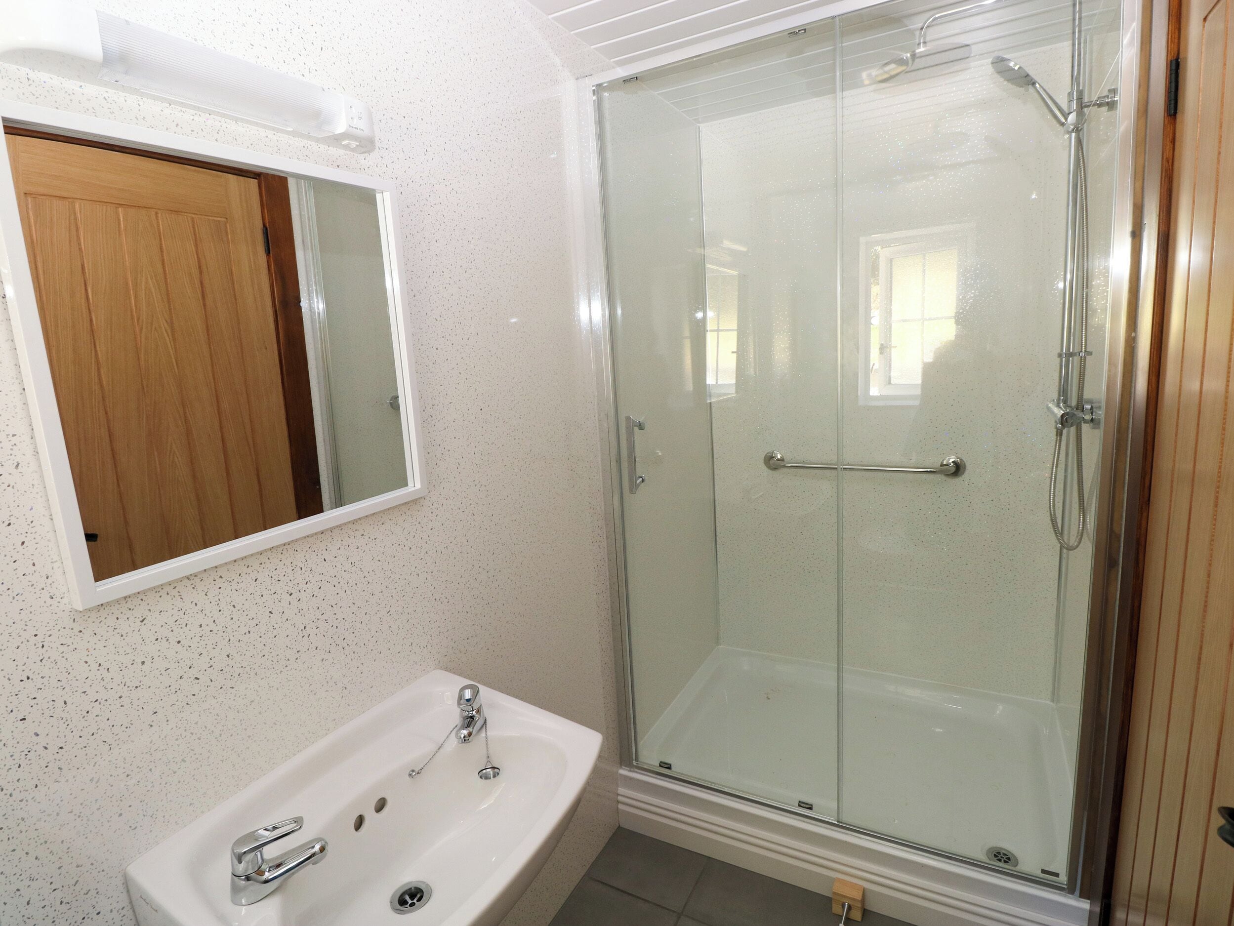 Un baño con ducha de vidrio, un lavamanos blanco con grifería cromada y una puerta de madera.