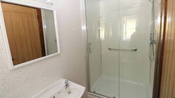 Un baño con ducha de vidrio, un lavamanos blanco con grifería cromada y una puerta de madera.