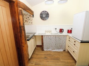 Eine kleine Küche mit Holzschränken, einer weißen Arbeitsplatte, einem roten Wasserkocher und einer Uhr an der Wand.