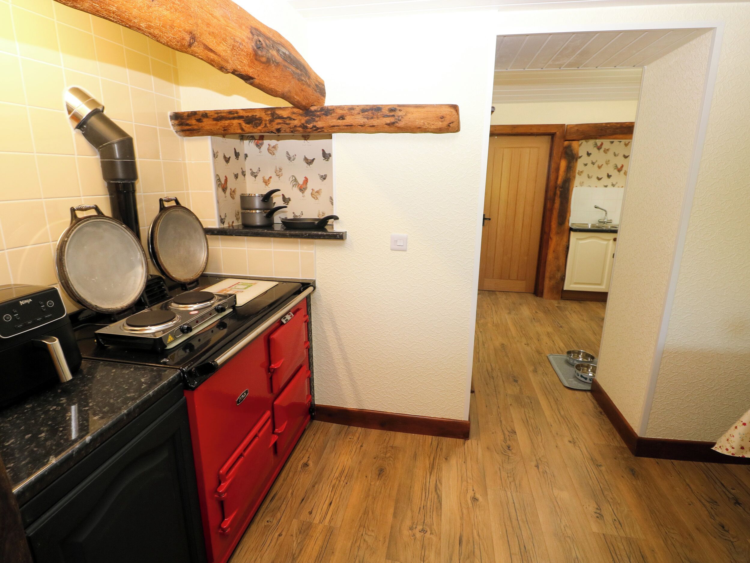 A kitchen with a red stove, a black range hood, and a wooden ceiling beam.