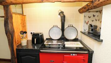 Una cocina con una estufa AGA roja, dos sartenes, una tetera eléctrica negra y un armario de madera.