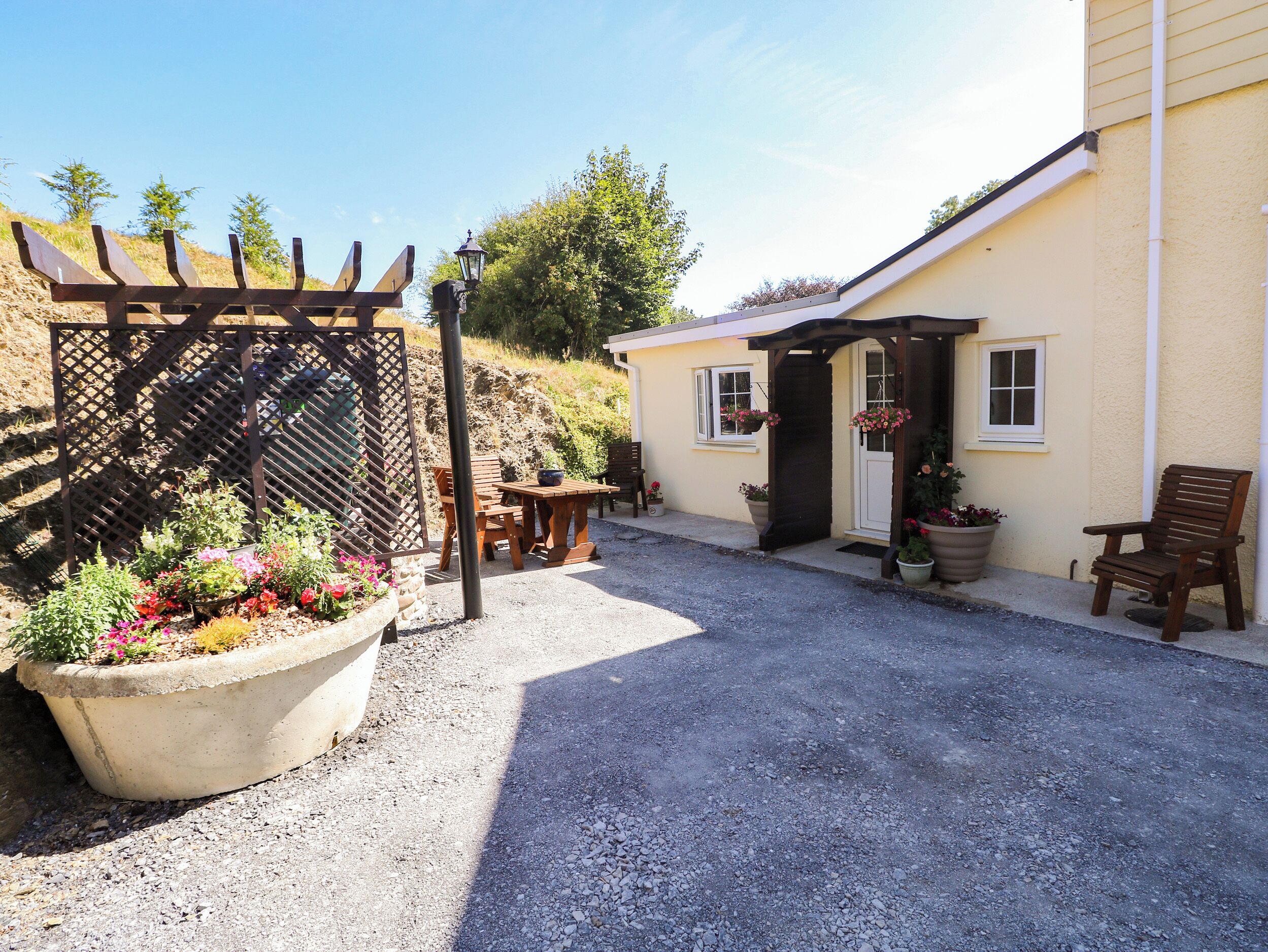 A gravel driveway leading to a house with a wooden pergola and potted plants.