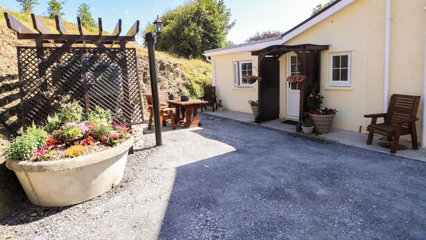 Ein unbefestigter Weg führt zu einem Haus mit einer Holzpergola und Topfpflanzen.
