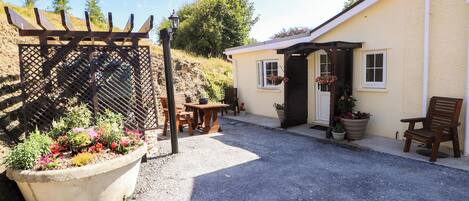 A gravel driveway leading to a house with a wooden pergola and potted plants.