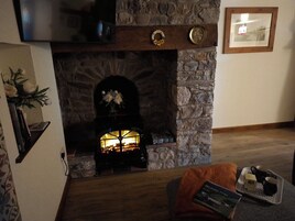 Una chimenea de piedra con fuego, un cuadro enmarcado en la pared y un libro sobre una bandeja.