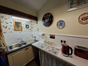 A kitchen with a sink, a kettle, and a toaster. There are decorative plates and a clock on the wall. - Dolcoed (Llandeilo)