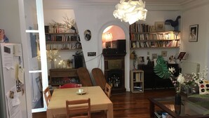 Een gezellige woonkamer met een eethoek, boekenkasten, een open haard en een salontafel met decoratieve objecten.