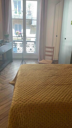A room with a bed, a chair, a desk with a computer, and a balcony with a view of the outside. - Beautiful, quiet apartment in the heart of the 9th arrondissement (Paris)